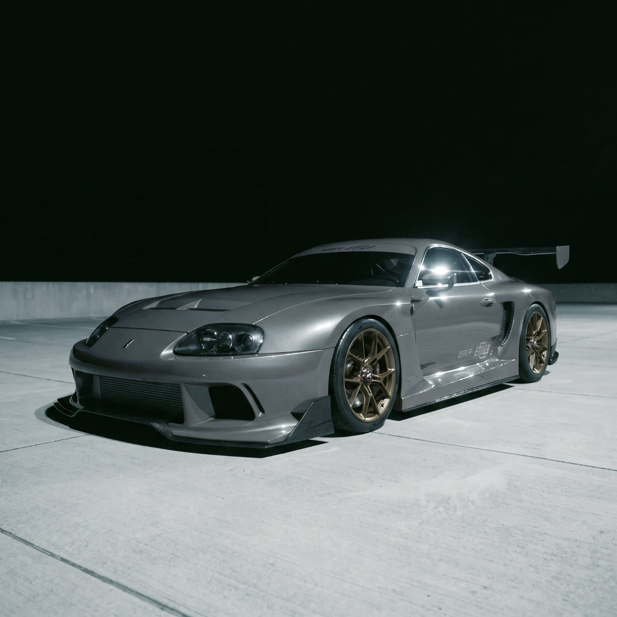 Gray Toyota Supra A80 with the ETi MK4 Supra Widebody kit in a parking structure, front three-quarter view, render